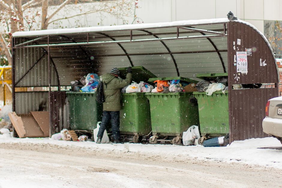 In the foreground, there is a large pile of mixed waste materials, including cardboard boxes, plastic containers, and paper supplies, all stacked haphazardly on a paved surface outside a building. The